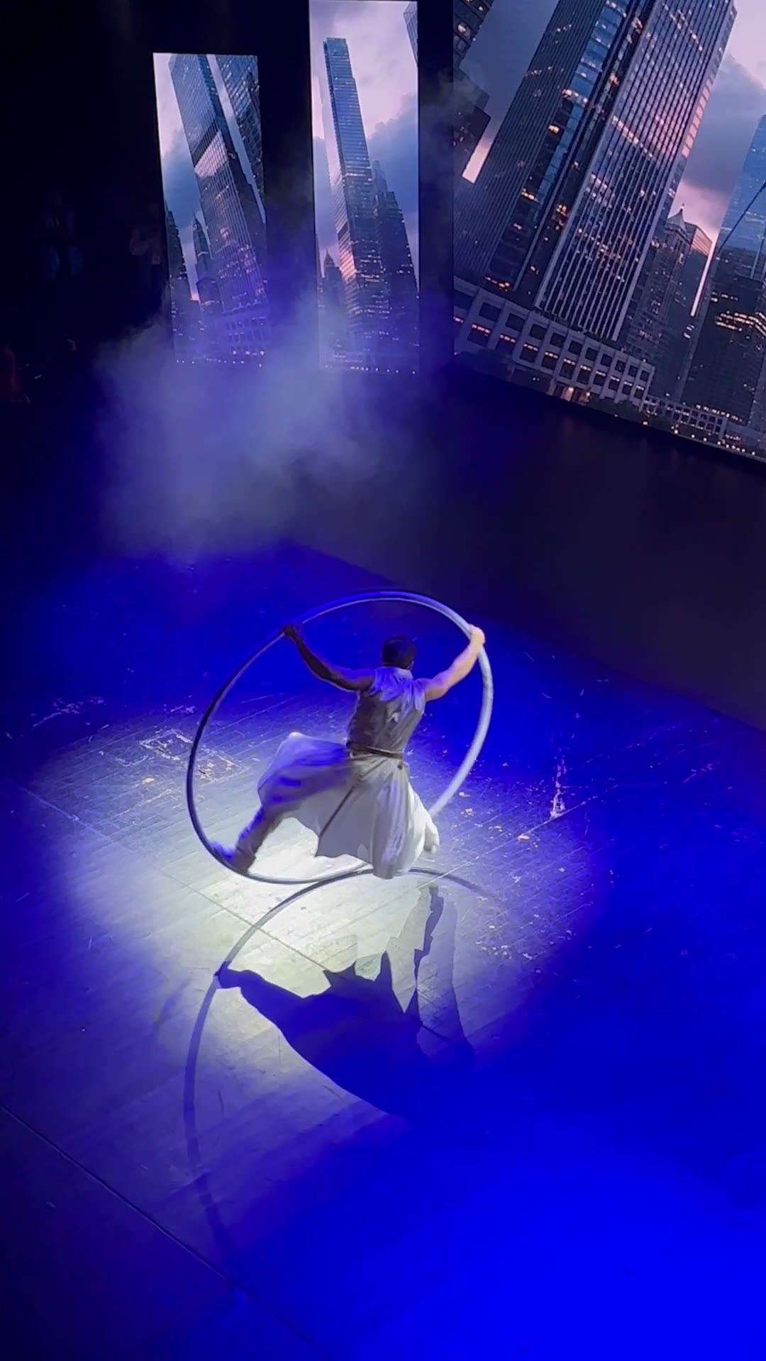 Mavi ışıklı sahnede Cyr Wheel içinde dönen performansçı
