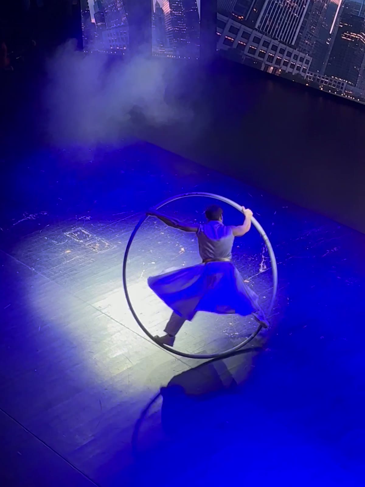 Mavi ışıklı sahnede Cyr Wheel çemberi içinde denge kuran sanatçı